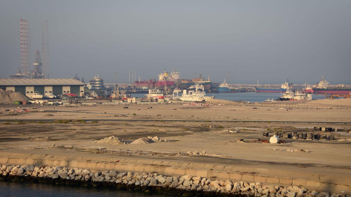 Tankers, a jack-up rig and support vessels moored along a commercial waterfront at dusk